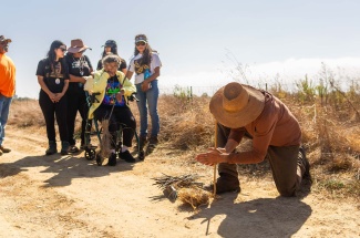 ayne Chapman uses a hand drill to start a coal, which Chumash Elder Ernestine Ygnacio-De Soto (seated) will use to start the fire.