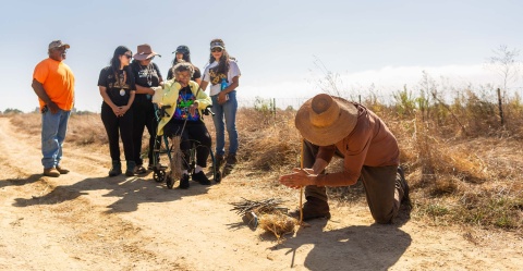 ayne Chapman uses a hand drill to start a coal, which Chumash Elder Ernestine Ygnacio-De Soto (seated) will use to start the fire.